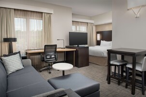 A hotel room with a sofa, a desk with a computer, a TV, a bed, and a small table with two chairs.