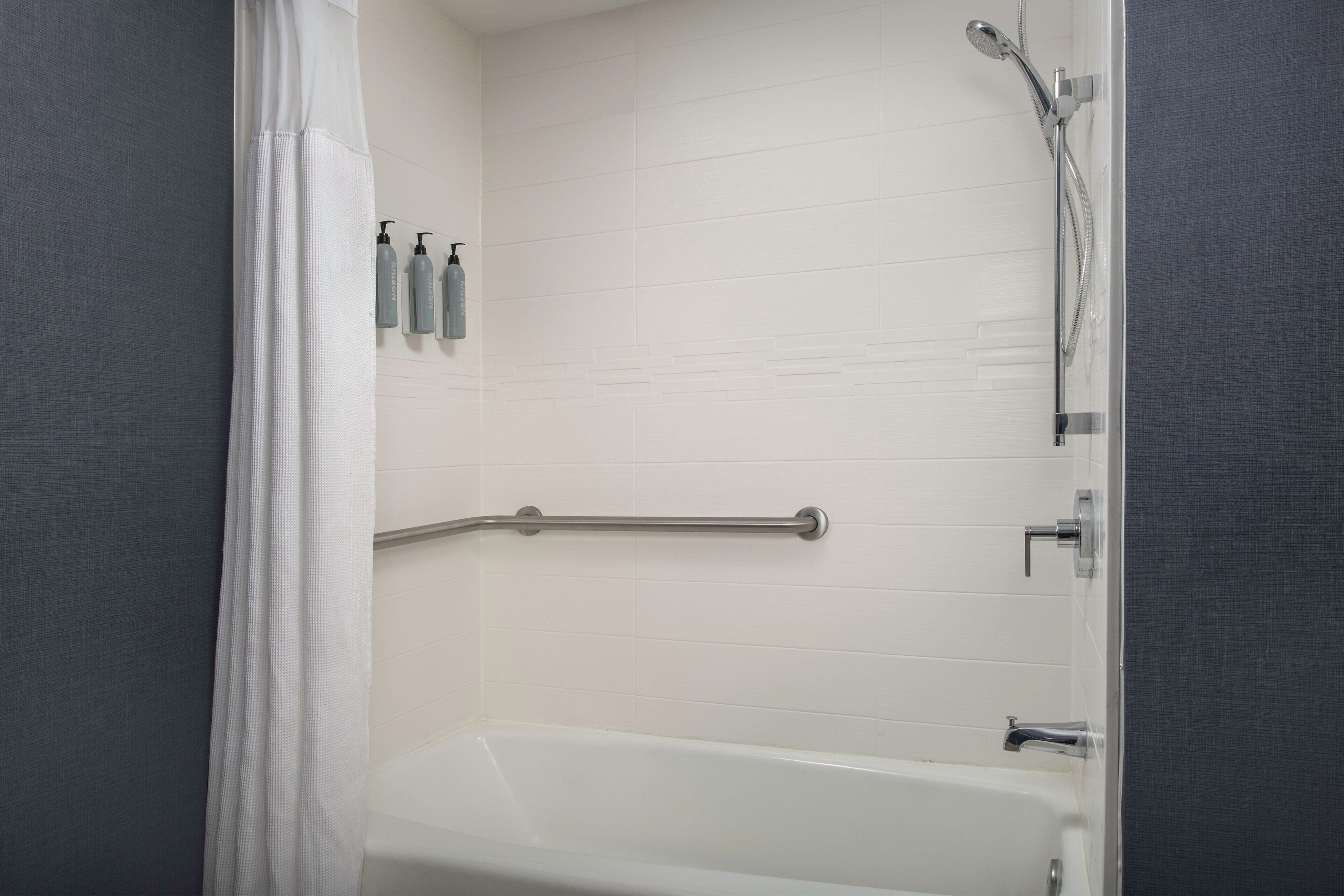 A bathroom with a bathtub, a shower, and a grab bar.