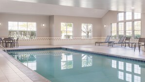Una piscina interior con agua cristalina y azul, rodeada por una terraza de azulejos y equipada con sillones de descanso.