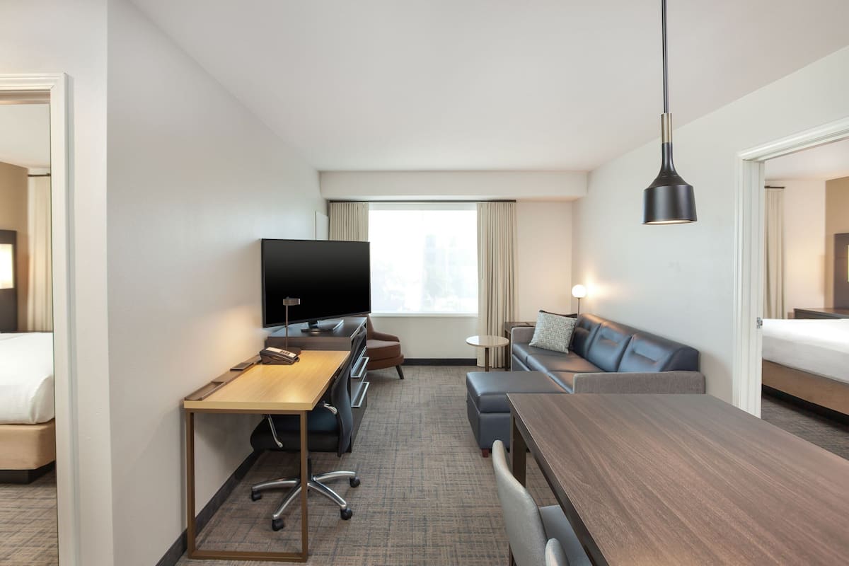 A hotel room with a bed, a desk with a computer, a television, a sofa, and a dining table.