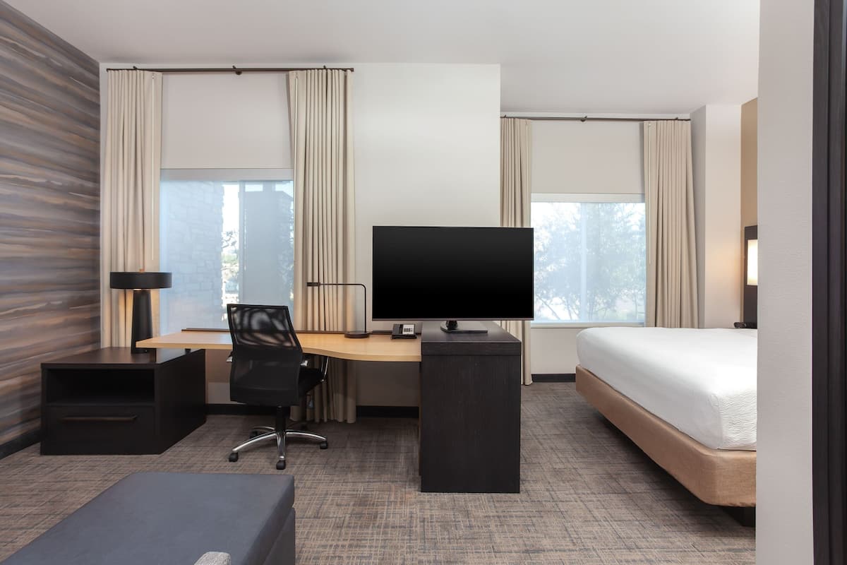 A hotel room with a bed, a desk with a computer, a chair, and a TV.