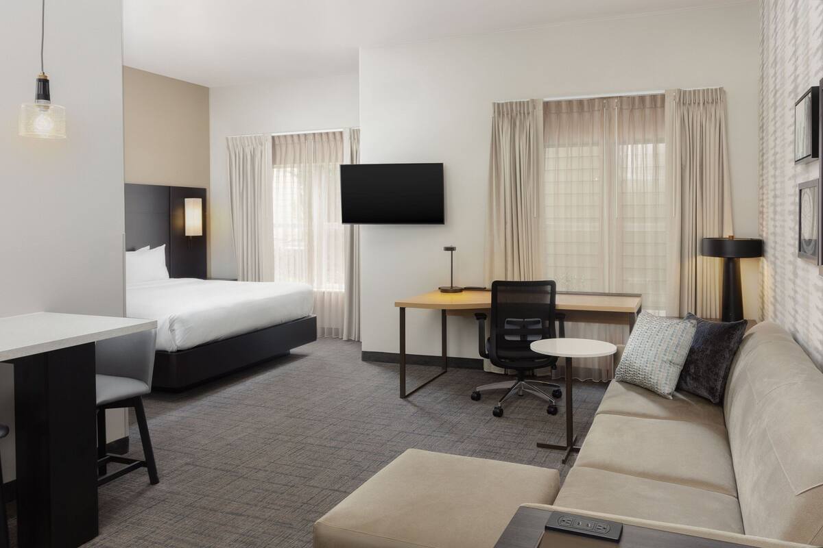 A hotel room with a bed, a desk, a chair, a sofa, and a TV.