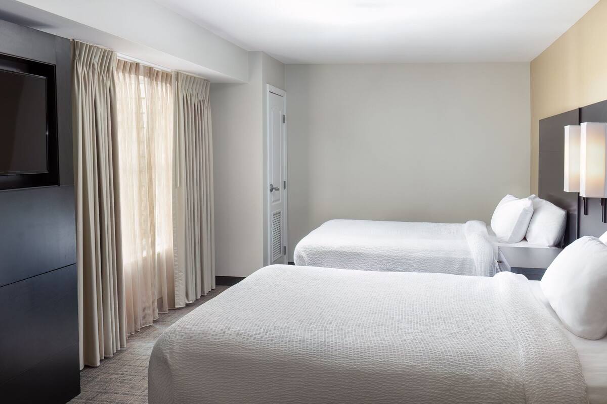 A hotel room with two beds, a TV, a lamp, and a door.