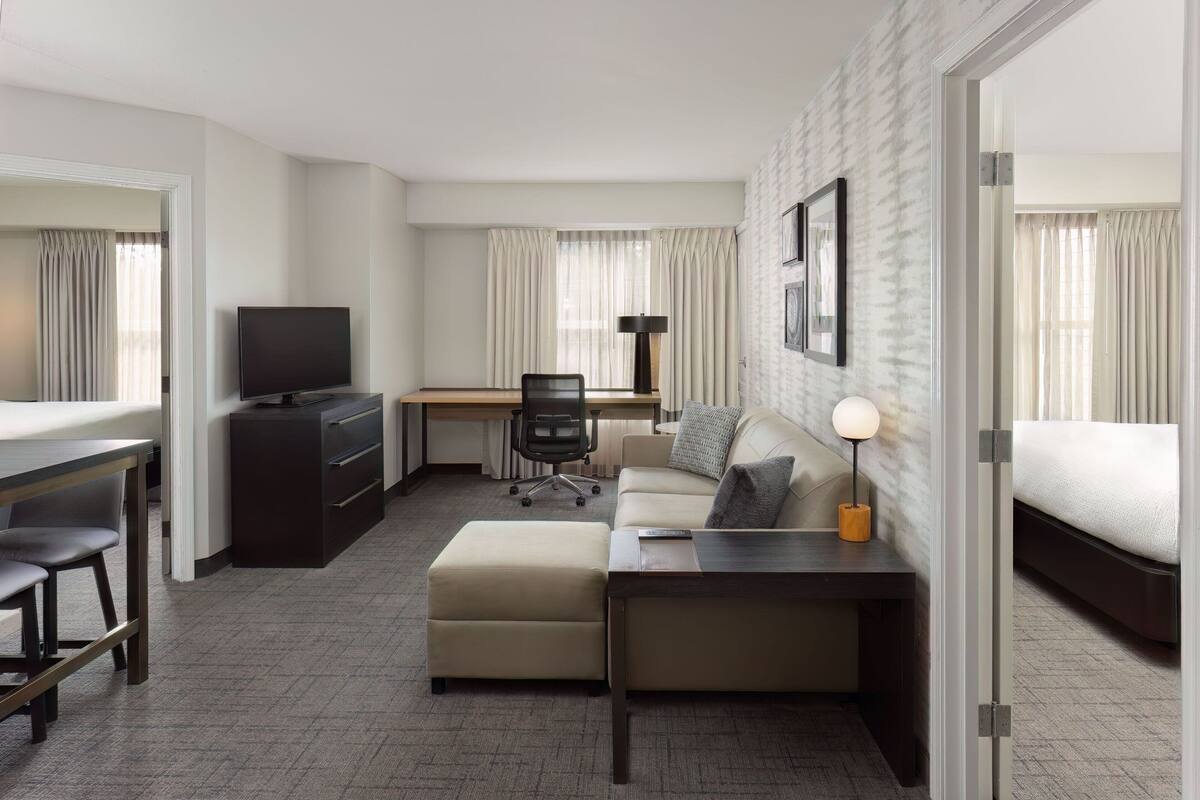 A hotel room with a bed, a desk with a chair, a sofa, a TV, and a lamp.
