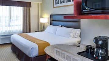 A hotel room with a bed, desk, chair, television, and a coffee maker.