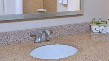 Un baño con encimera de granito, un lavabo blanco, un espejo y artículos de aseo en una bandeja.