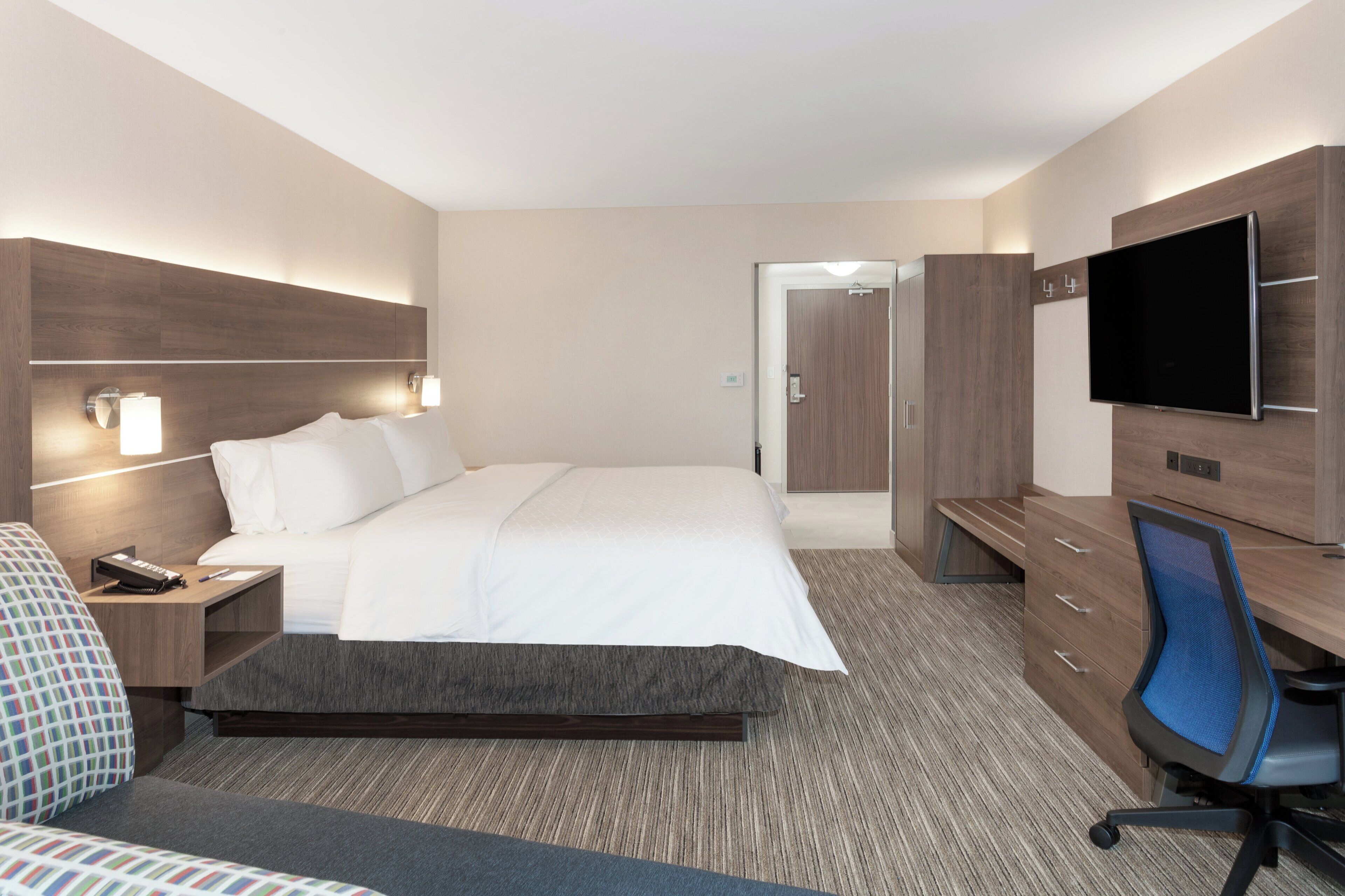 A hotel room with a bed, bedside tables, a desk with a chair, a television, and a wardrobe.