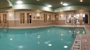 Una piscina interior con agua cristalina, rodeada de paredes con ventanas y puertas, y un suelo de baldosas.