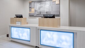 Un mostrador de recepción con dos computadoras HP, una obra de arte moderna en la pared y un expositor iluminado.