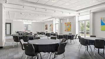 Una amplia sala de conferencias con mesas y sillas redondas, ventanas grandes y obras de arte en las paredes.
