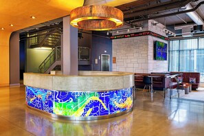 A modern lobby with a central reception desk, a staircase, and a digital display board.