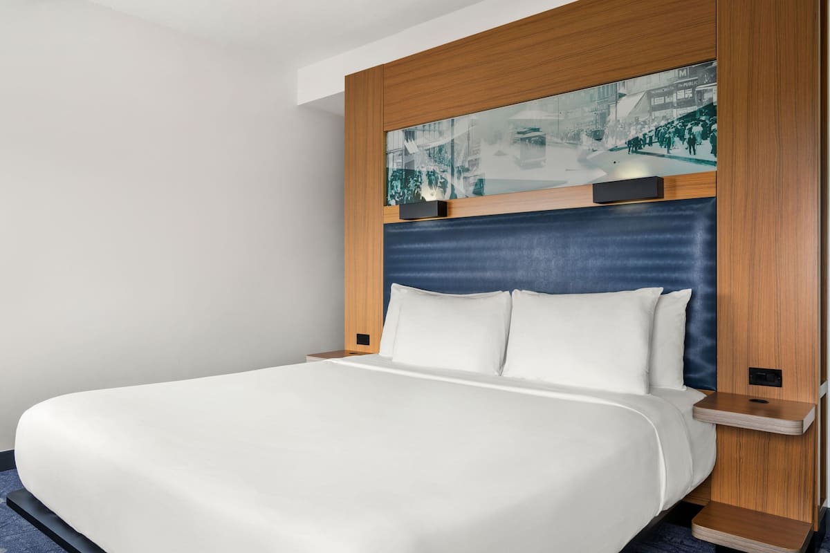 Quarto de hotel moderno com uma cama grande, cabeceira de madeira e uma fotografia de paisagem urbana acima da cama.
