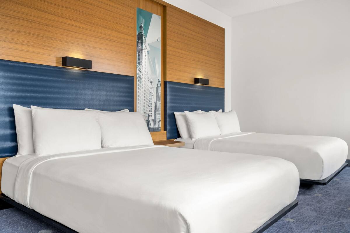 Quarto de hotel com duas camas, cabeceiras de madeira e uma grande pintura com vista da cidade na parede.