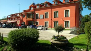 Un edificio rojo con múltiples ventanas y balcones, un estacionamiento con coches y un pequeño jardín con un árbol y flores.