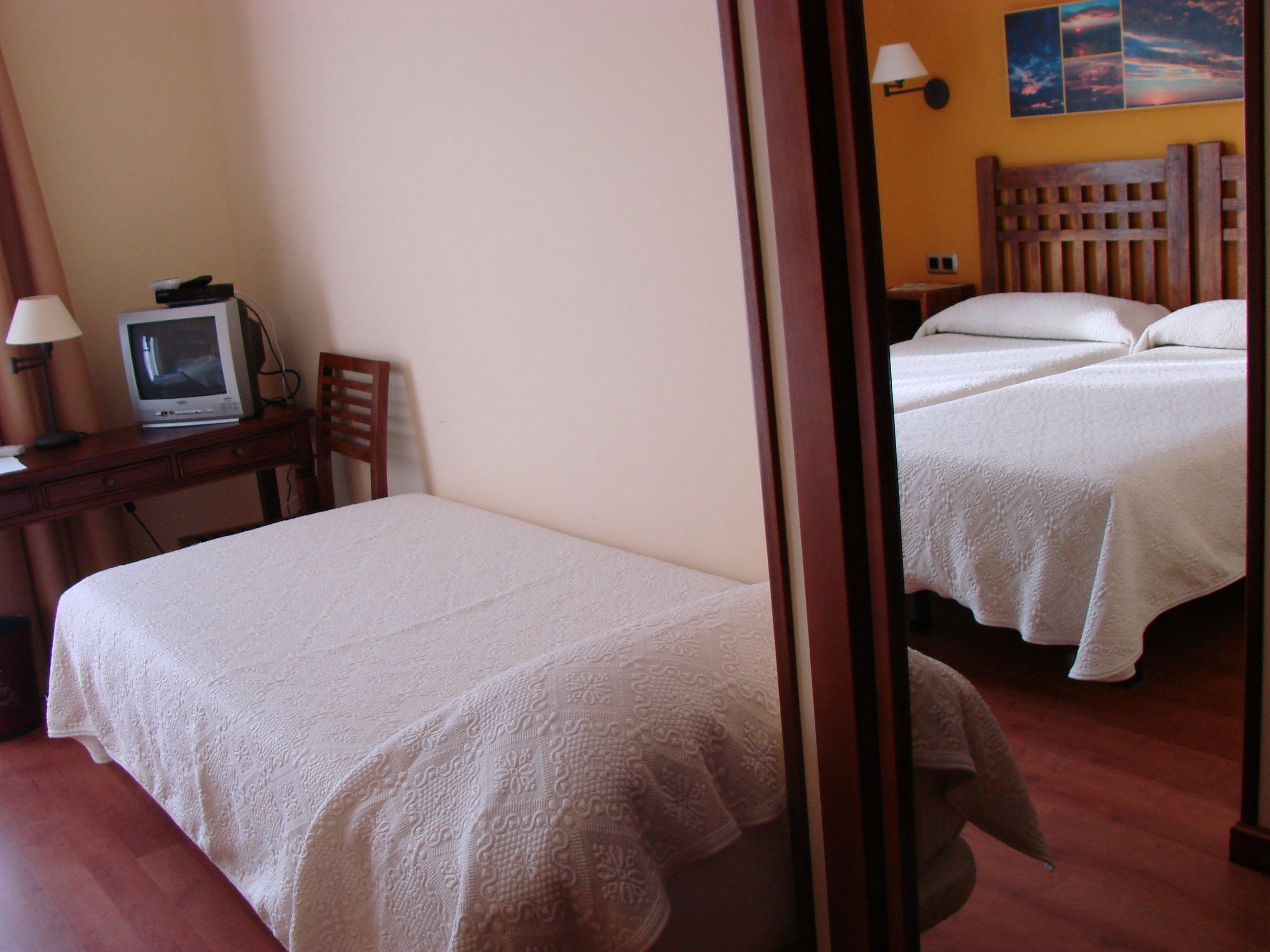 Une chambre d’hôtel avec un lit simple, un bureau avec une télévision et une table de chevet.