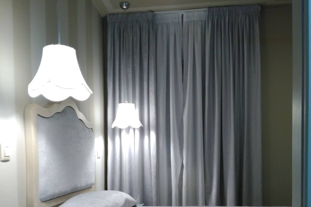 Une chambre à coucher avec un lit, une table de chevet, une lampe et une fenêtre avec des rideaux.