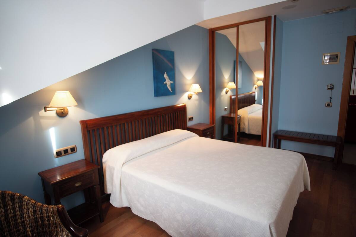 Une chambre d’hôtel comprenant un lit, des tables de chevet, une chaise, un miroir et une lampe fixée au mur.