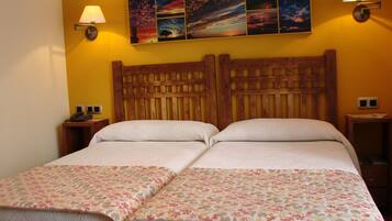 Ein Doppelbett mit blumigem Bettbezug, ein hölzernes Kopfteil, zwei Nachttischlampen und ein an der Wand hängendes Kunstwerk, das einen Sonnenuntergang zeigt.