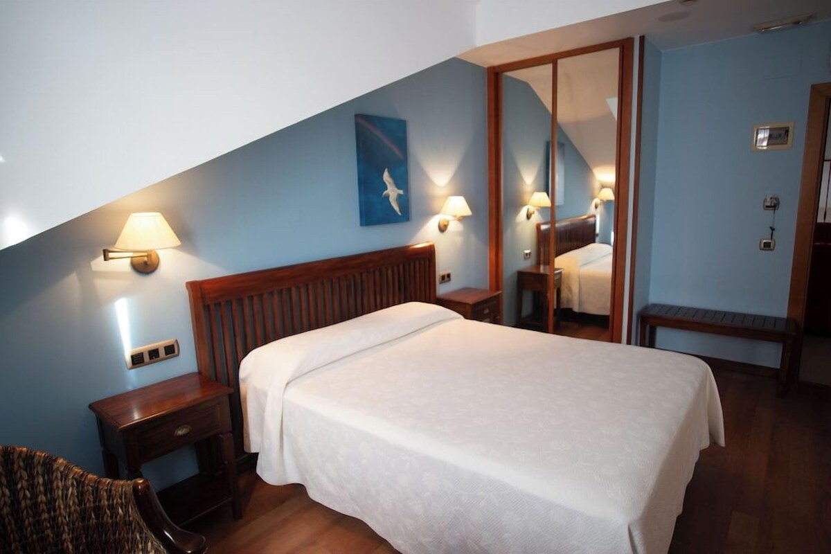 Une chambre d’hôtel comprenant un lit, des tables de chevet, une chaise, un miroir et des lampes fixées au mur.