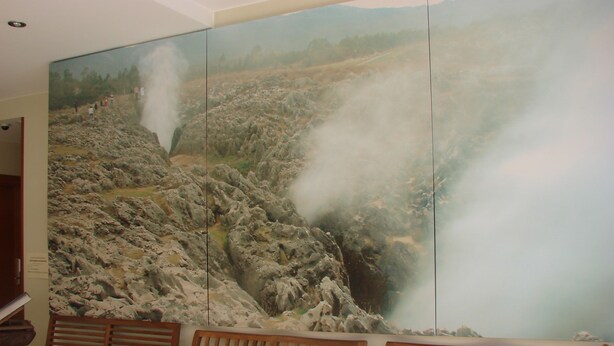 Una habitación con bancos de madera y un gran mural en la pared que muestra un paisaje rocoso con vapor.