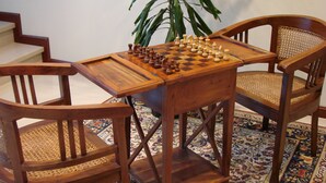 Una mesa de madera para jugar ajedrez con sillas, una planta y una alfombra estampada.