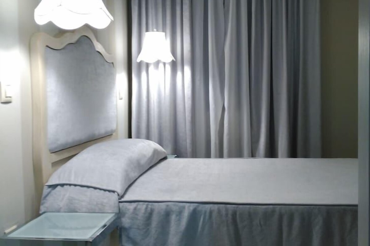 Une chambre à coucher avec un lit, deux lampes de chevet, une table de nuit et une fenêtre avec des rideaux.