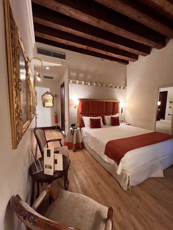 A hotel room with a large bed, a wooden ceiling, a desk with a chair, and a mirror.