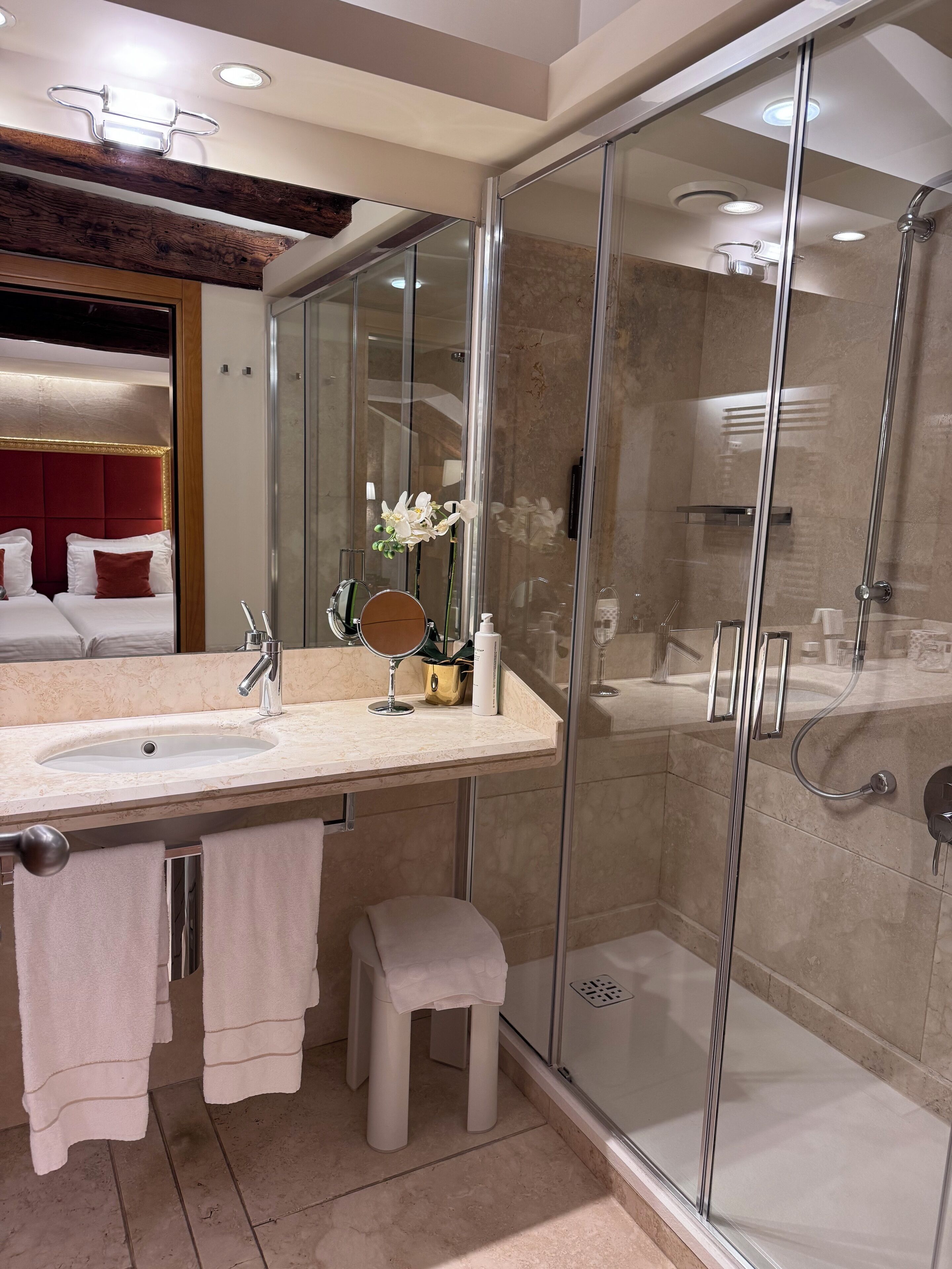 Une salle de bain moderne avec une douche à parois de verre, un meuble-lavabo avec un miroir et un petit tabouret.