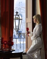 Una stanza con vista su un edificio, un tavolo con bicchieri di vetro rossi e una persona che tiene in mano un bicchiere rosso.