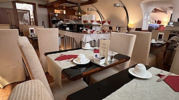 A hotel dining area with tables set for two, featuring a modern design with neutral tones and a central island.