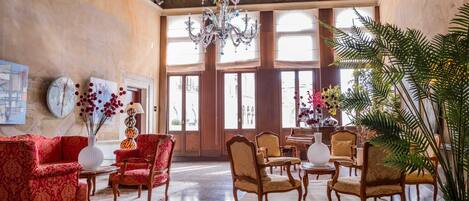 A spacious lobby with a grand chandelier, elegant furniture, and large windows allowing natural light.