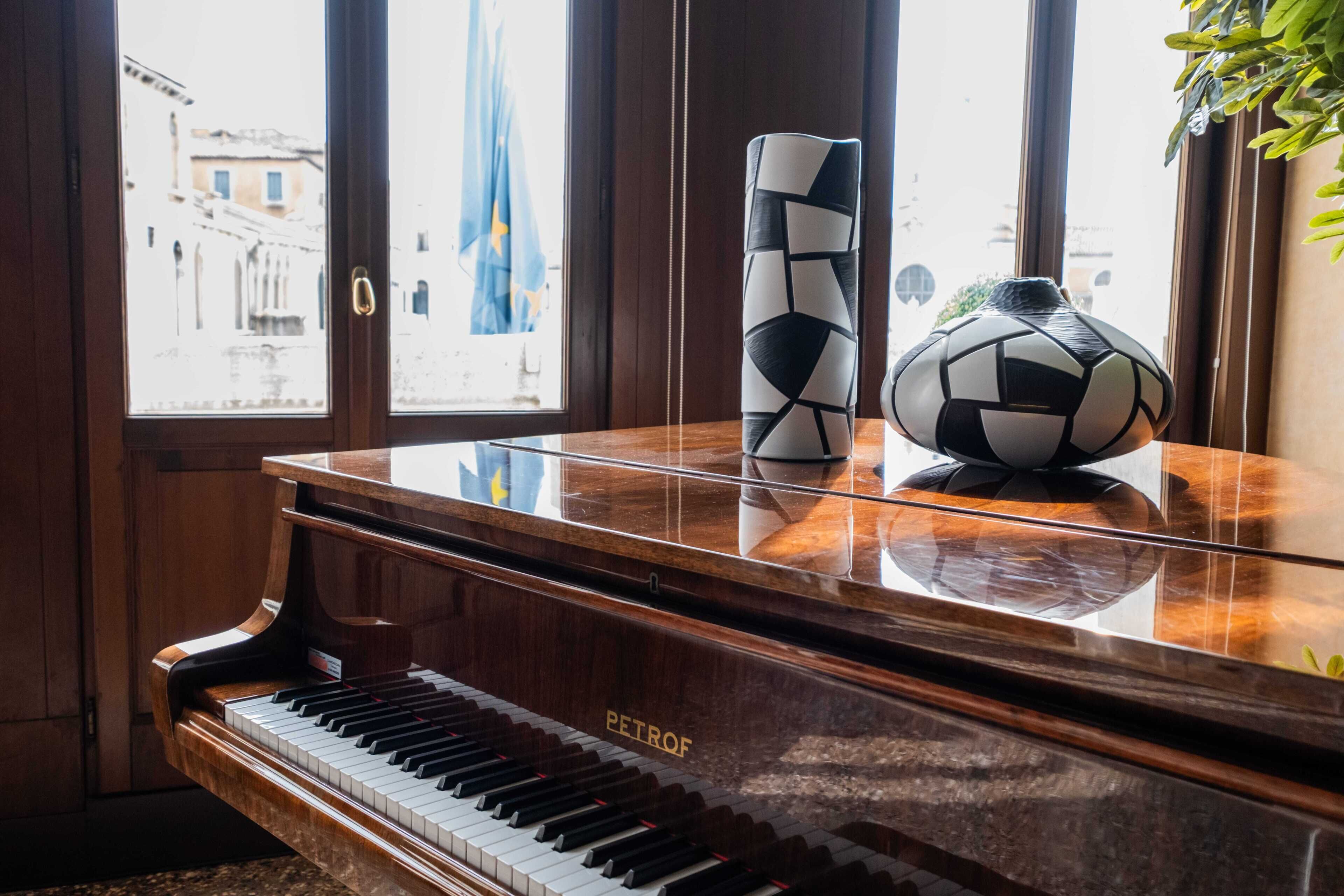 A grand piano with a reflective surface, a decorative vase, and a soccer ball on top.