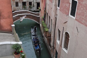 A narrow canal with a gondola carrying passengers, flanked by historic buildings with arched windows and balconies.