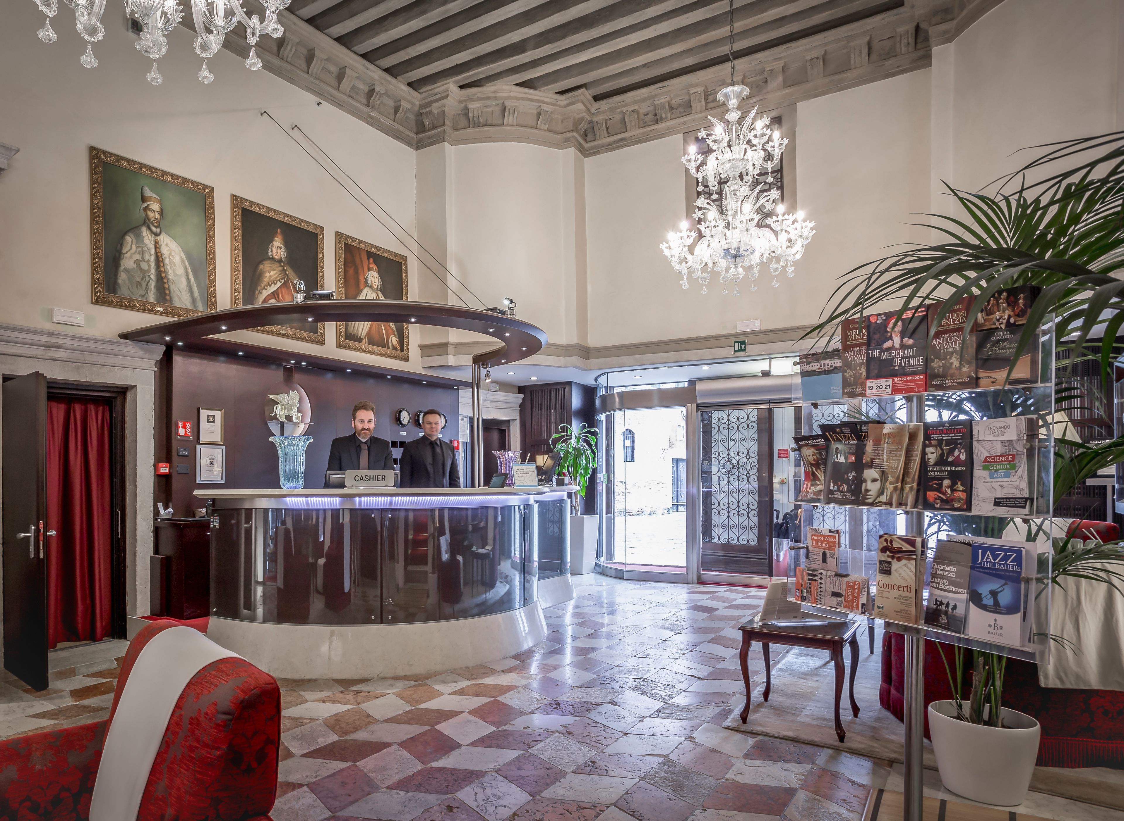 A hotel lobby with a reception desk, a chandelier, framed artwork, and a book display.