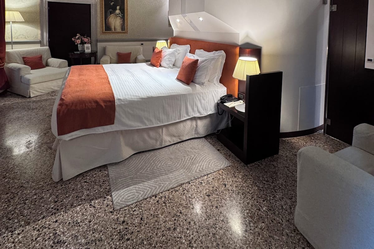 A modern hotel room with a large bed, a nightstand, a desk, and a chair.