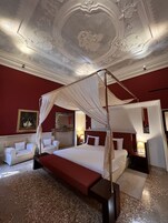 Ein luxuriöses Schlafzimmer mit Baldachinbett, einer roten Akzentwand und aufwendigen Deckenverzierungen.