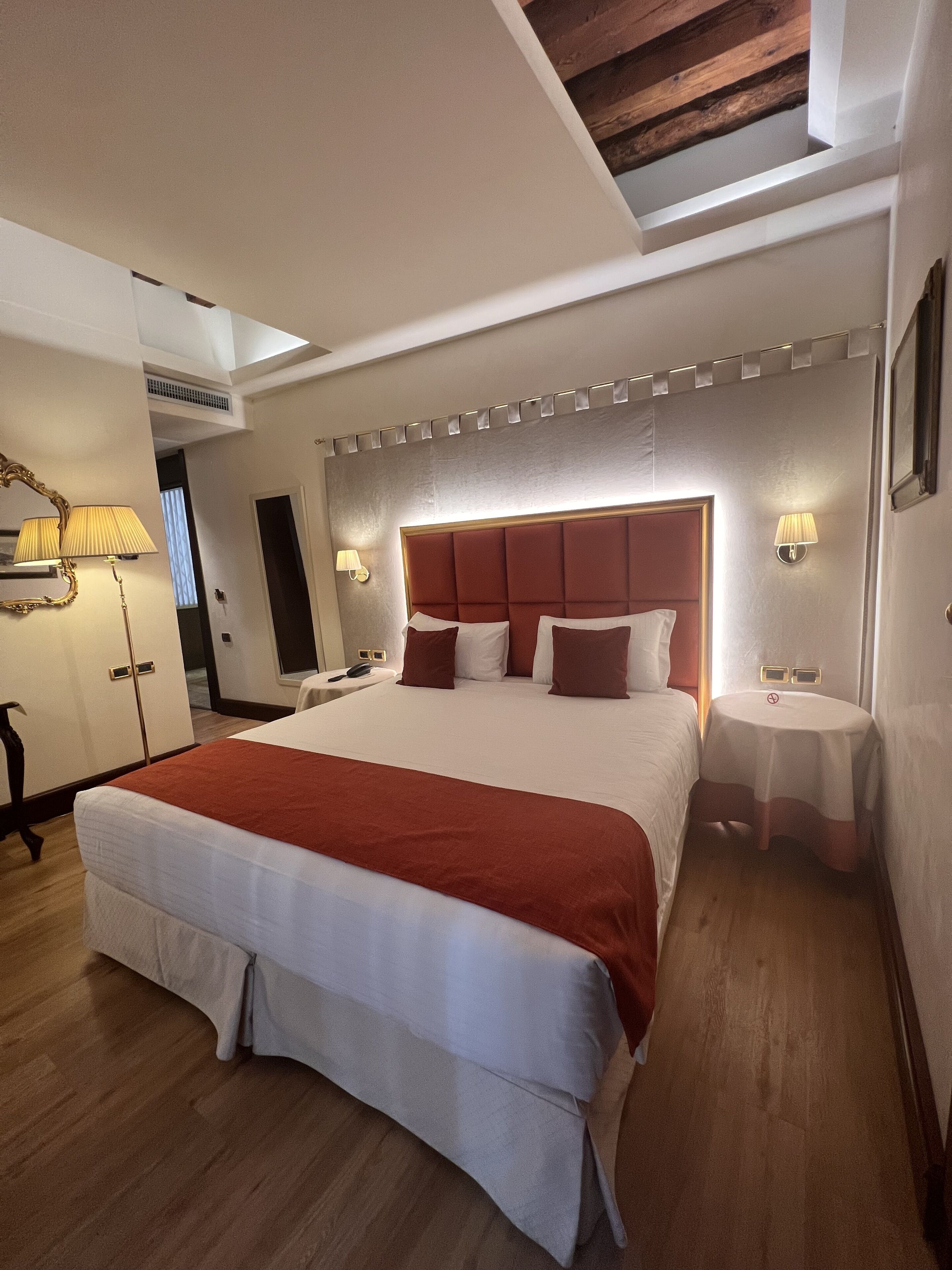A hotel room with a large bed, bedside tables, a mirror, and a ceiling light.