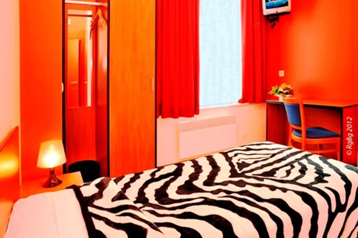 Una camera d'albergo con una coperta a motivi zebrati, pareti rosse, un armadio in legno, una scrivania con una sedia e una televisione a parete.