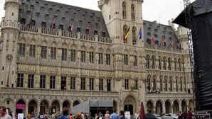 A historic building with a large central tower and multiple flags. - Hotel The Moon (Brussels)