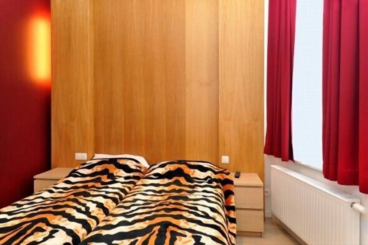 Una camera da letto con una testiera in legno, un letto con coperta a motivi zebrati, due comodini e tende rosse.