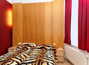 A bedroom with a wooden headboard, a bed with a zebra-patterned blanket, two bedside tables, and red curtains. - Hotel The Moon (Brussels)