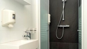 A modern bathroom with a glass-enclosed shower, a white sink, and a soap dispenser. - Hotel The Moon (Brussels)
