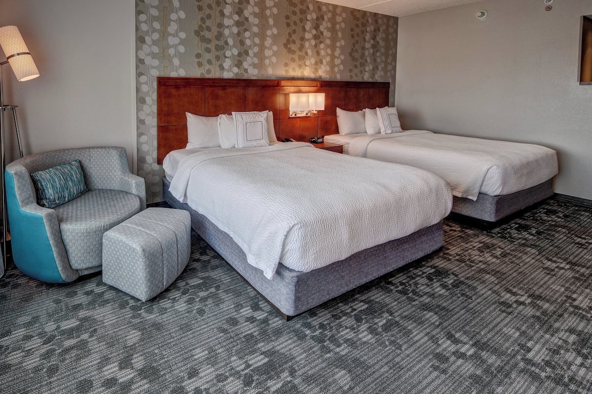 Habitación de hotel con dos camas, una silla y una mesita de noche.