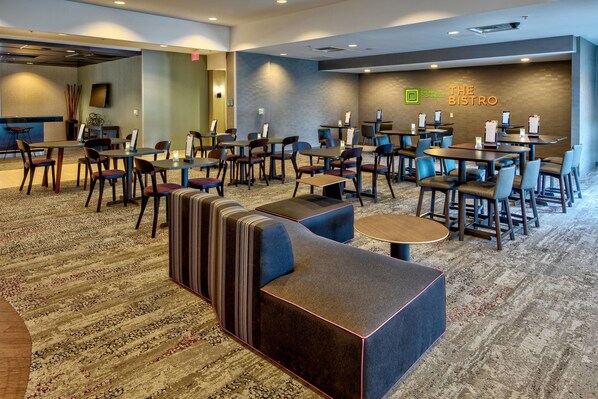 Un hall de hotel con diversas opciones de asientos, incluyendo sitiales y mesas, una alfombra estampada y un letrero en la pared que dice "The Bistro".