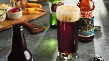 Una cerveza en un vaso, una botella de cerveza Ballast Point y una botella de cerveza Liguus sobre una superficie metálica.