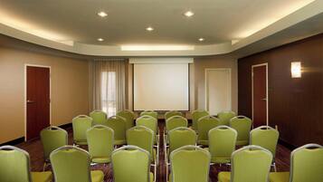 A conference room with rows of green chairs, a large projection screen, and a wooden door on the right.