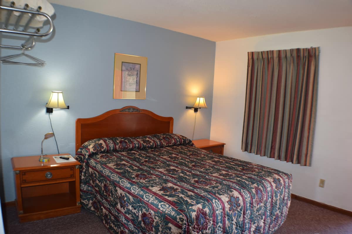A bedroom with a wooden bed, two bedside tables, a nightstand, a hanging clothes rack, and a window with curtains.