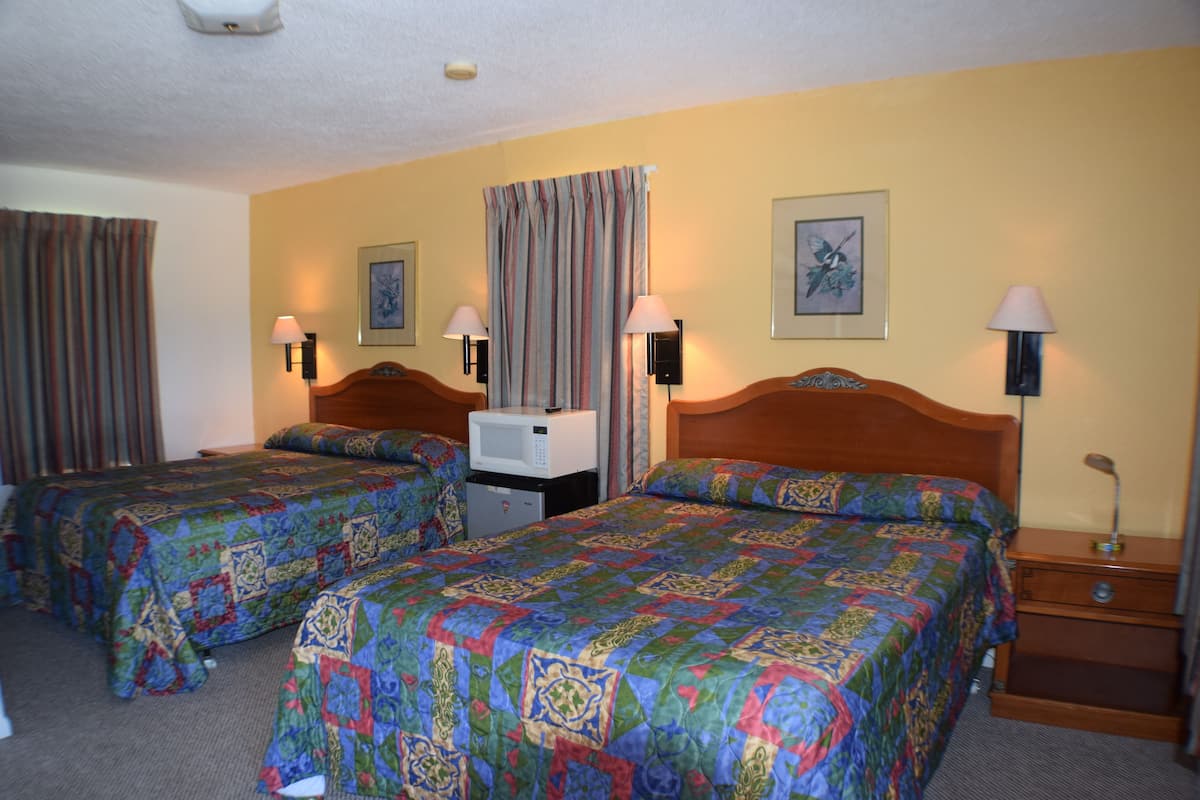 A hotel room with two beds, a microwave, and a nightstand with a lamp.