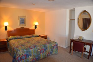 A hotel room with a bed, two bedside lamps, a desk, a chair, and a mirror. - Best Budget Inn (Carthage)