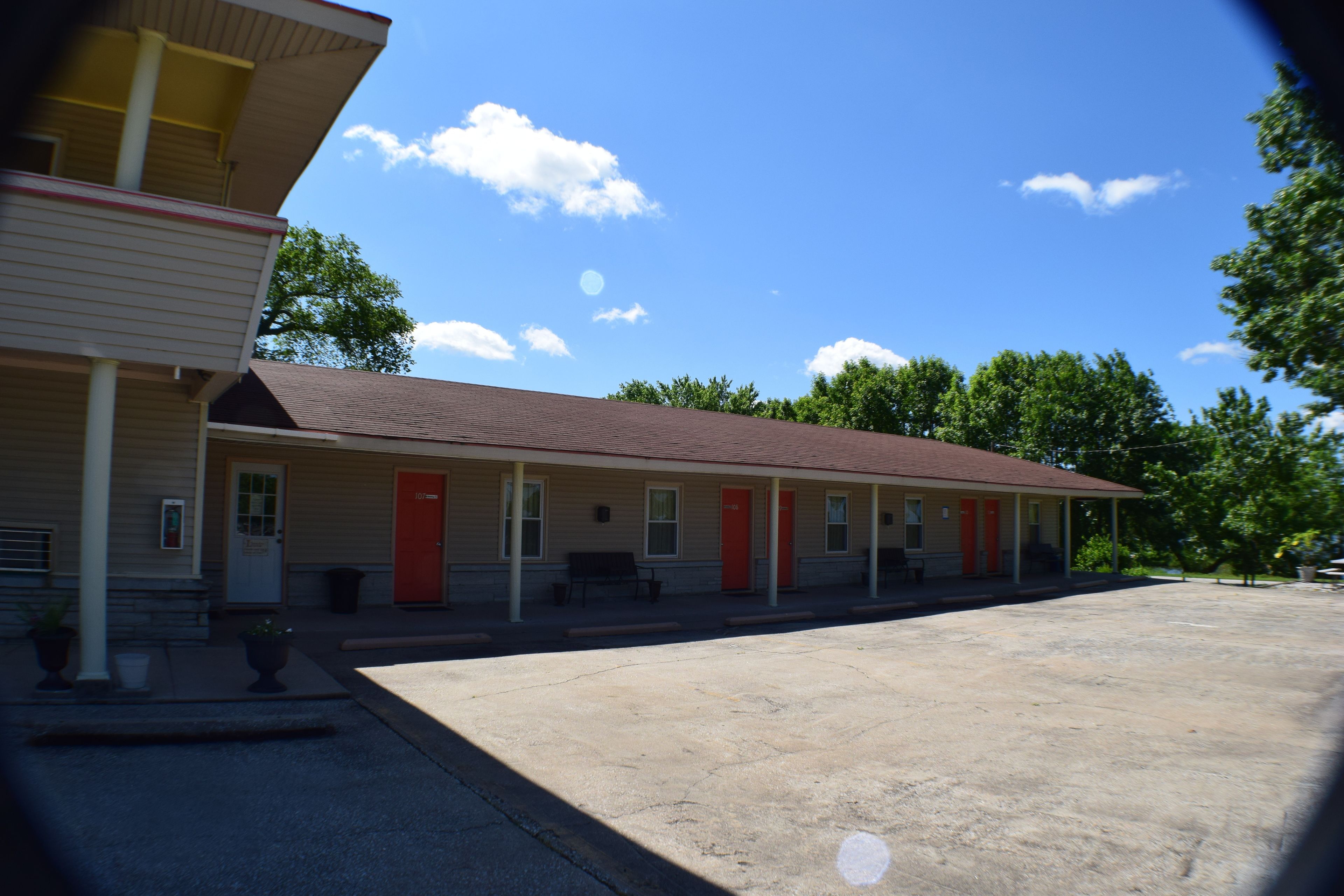 A motel with a row of rooms, a parking lot, and a clear blue sky.